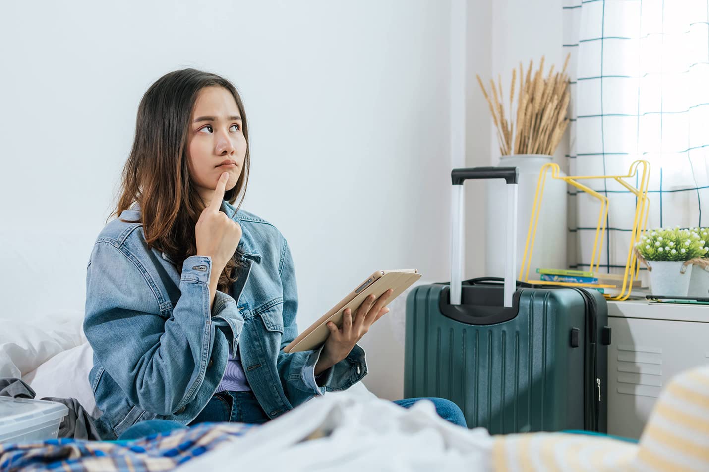 Considering Selling Clothes on Amazon Een vrouw zit op bed met een tablet en denkt na over het verkopen van kleding op Amazon.