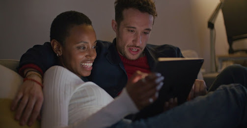 2 mensen kijken naar media op een tablet terwijl ze op de bank zitten.